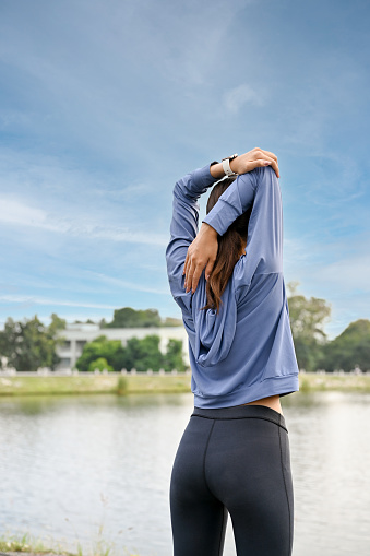 Healthy Asian woman in sportswear stretching her arms and shoulders, warming up or cooling down, getting ready to exercise. back view.