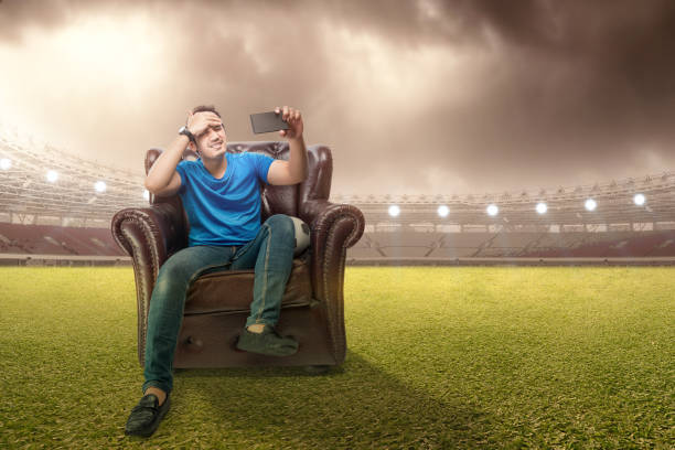 istock Asian man with the ball sitting on the couch with a disappointed expression watching a football match from a mobile phone 1450465358