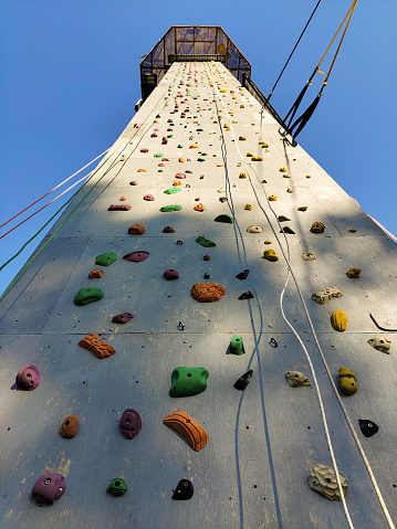 Sports climbing wall in perspective with various hooks, hanging rope belay. View from below on the background of the sky