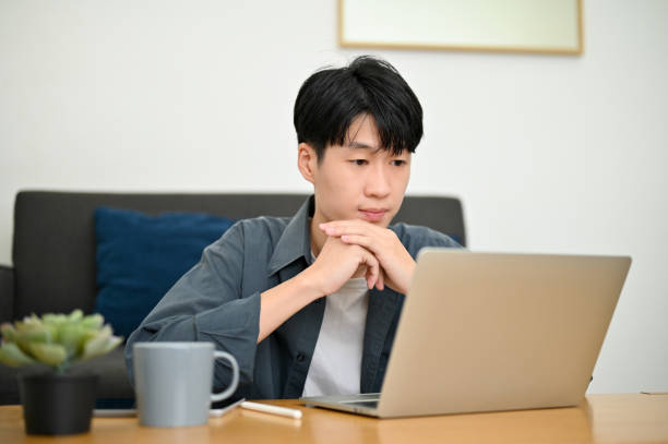 istock Smart Asian male hands on chin, looking at his laptop screen, thinking about his project. 1450513730