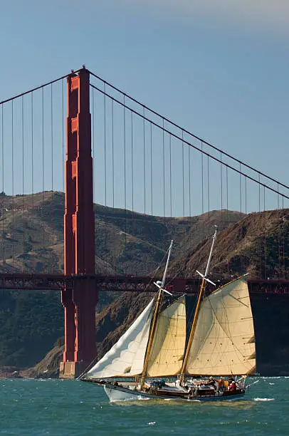 A beautiful antique sailboat tacks in the shadow of the Golden Gate Bridge before setting sail on a Pacific Ocean cruise.