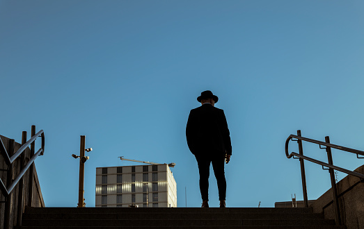 Silhouette of adult man in suit and hat standing on stairs against blue sky