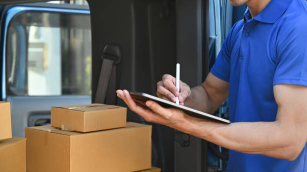 istock Cropped shot of delivery man in blue uniform using digital tablet next to open delivery van. Shipping and delivery service concept. 1450533613