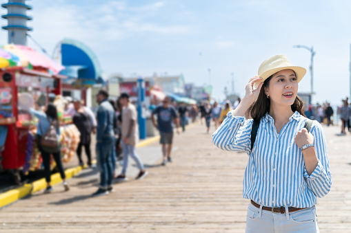 happy asian Korean female visitor wearing hat enjoying view near treat carts on street at santa monica pier in California usa
