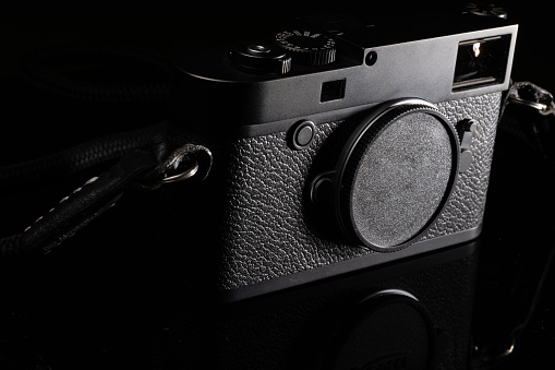 A rangefinder classic camera placed on reflective material. Dark backdrop.