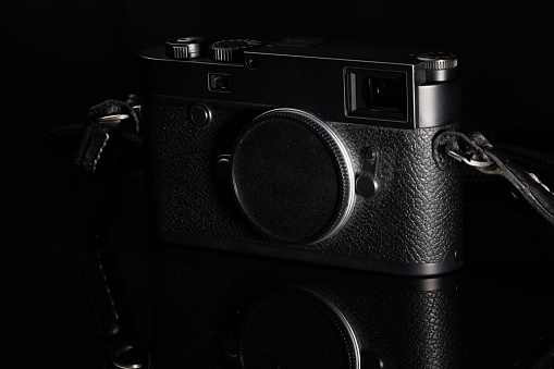 A rangefinder classic camera placed on reflective material. Dark backdrop.