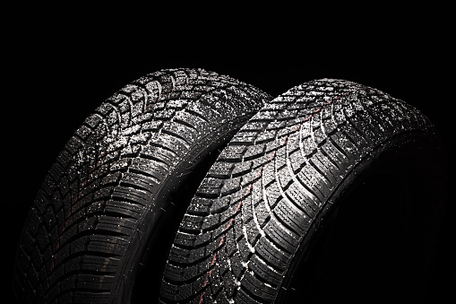 Winter Car tire with snow on black background. Tyre and snowflakes with copy space for text.