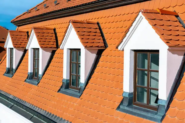 Old dormer windows on red tiled roof of historical house on sunny day