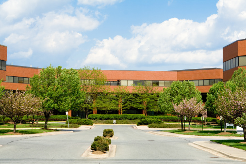 Sprawling red brick office building in suburban Maryland, United States.  Building is set back from the road, and has low trees in front.  - See lightbox for more
