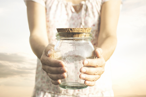 woman showing an empty glass jar that she holds in her hands, concept of economic crisis, savings, poverty