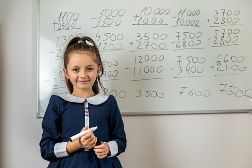 Little beautiful girl answers in front of the school blackboard smiling. school concept of education. school years