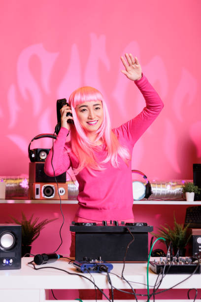 Smiling artist working as dj playing at mixer console, mixing techno music with eletronic using audio equipment. Performer with pink hair having fun in studio standing over pink background.