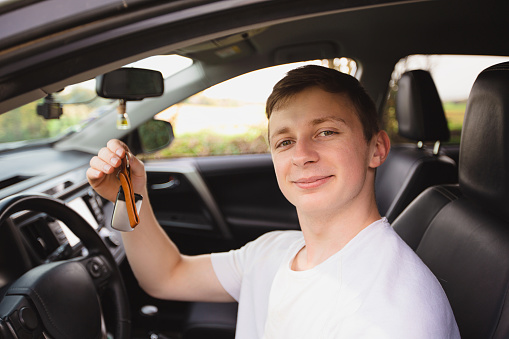 Smiling Novice driver holding car keys from his first car. New driver on the road concept.