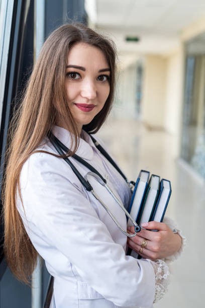 istock happy young nurse in uniform with stethoscope smiling in corridor. 1450558812