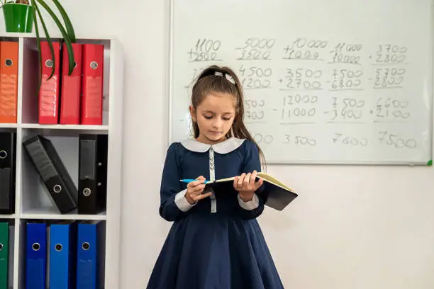 fleeting student stands by the blackboard with her notebook to see where to take an example. the student answers. school years. the best time