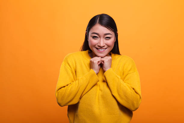 splendida donna asiatica felicissima che sorride di cuore mentre indossa un maglione vibrante su sfondo arancione. - 5502 foto e immagini stock