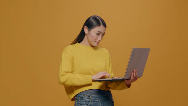 istock Asian woman using laptop in front of camera over yellow background 1450565738