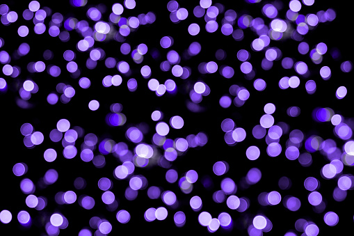 Abstract purple light beams background with bokeh and glowing particles.