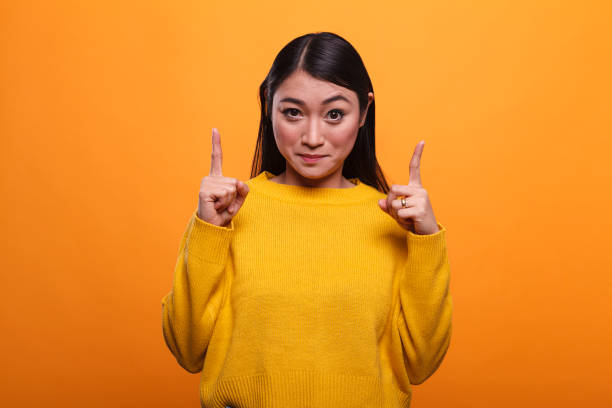 istock Confident woman pointing index fingers overhead while looking at camera 1450567031