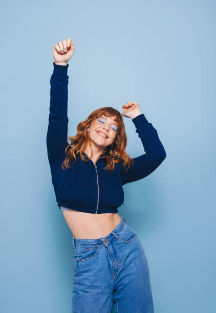 giovane donna felice che balla e si diverte indossando un crop top e jeans in uno studio - bassiera foto e immagini stock