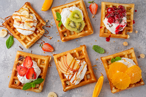 Homemade waffle with a cream, a variety of fruits, berries and sauces on a gray background. Traditional Belgian waffles. Top view