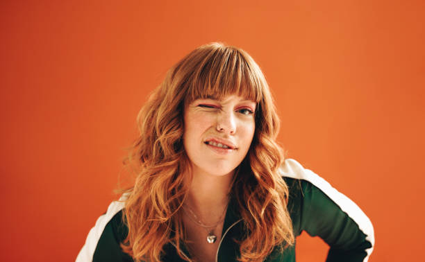 quirky young woman winking at the camera while standing in a studio - fashion women posing looking at camera imagens e fotografias de stock