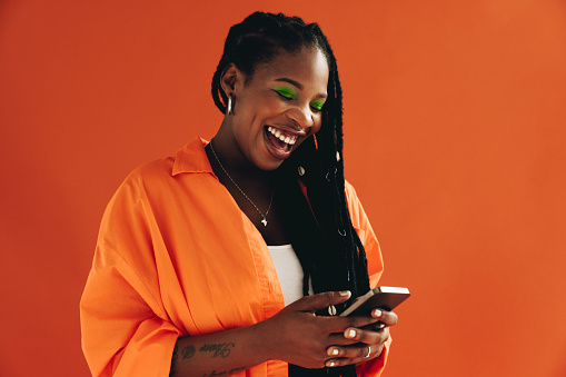 Black woman reading an exciting text message in a studio. Woman in casual clothing laughing while using her mobile phone.