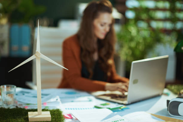 Wind turbine in green office and woman with laptop working stock photo