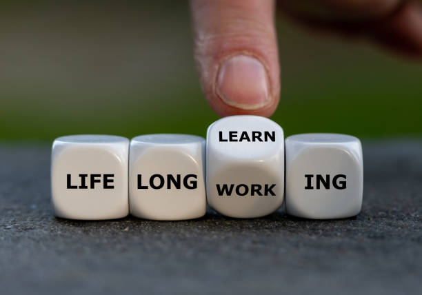Hand turns dice and changes the expression 'life long working' to ' life long learning'. stock photo