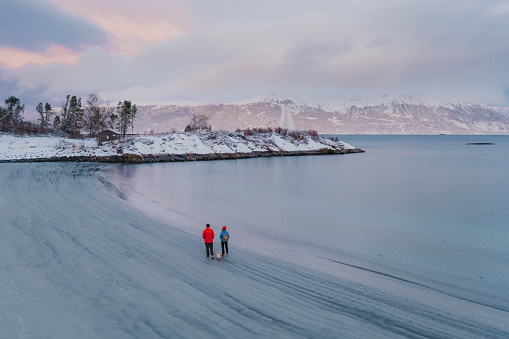 Aerial view woman and man walking at the scenic beach in snow in Norway