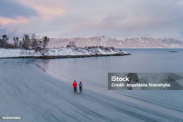 Aerial View Woman And Man Walking At The Scenic Beach In Snow In Norway Stock Photo - Download Image Now