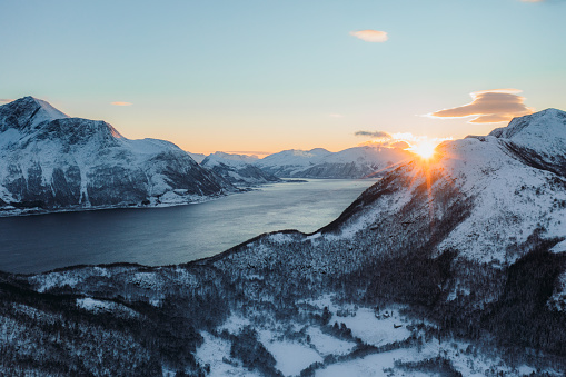 Drone high-angle photo of majesttic frozen colorful sunset above the snowy mountain peaks and the ocean in Western Norway