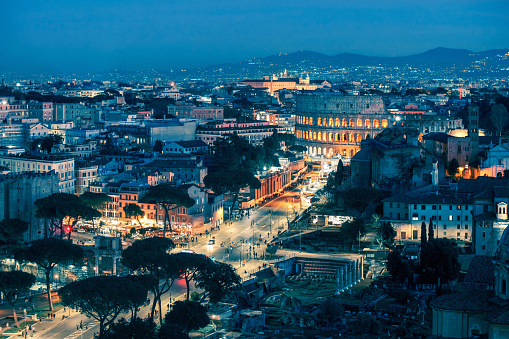 Rome by night: high angle view of Rome's historic downtown with the Coliseum surrounded by the old ruins of the Roman Forum, illuminated by street lights.