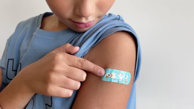 Child after vaccination with adhesive band-aid patch arm bandage to prevent any infection over white background. Positive concept of healthy lifestyle and care.