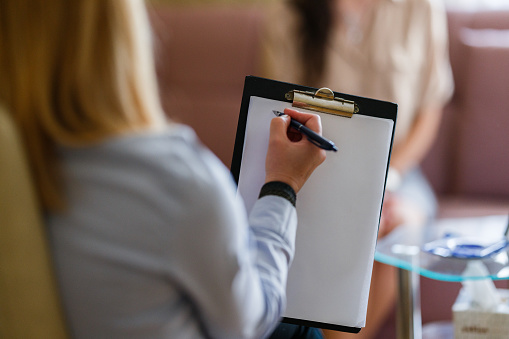 Close-up of a mental health counselor taking notes during a therapy session with a client in her office