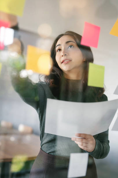 istock Young smiley attractive, businesswoman using post it notes in glass wall to writing strategy business plan to development grow to success 1450623065