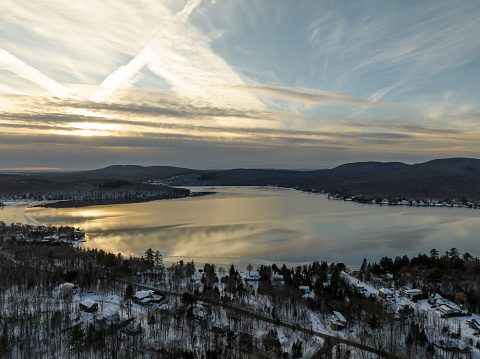 Aerial View of Lac St-Joseph in Winter Season, Quebec, Canada at Sunset.\n\nThe lake is frozen and there is no snow on the ice. The sun is reflecting on the ice and some cracks in the ice are visible.