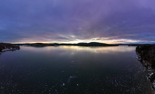Aerial View of Lac St-Joseph in Winter Season, Quebec, Canada at Sunset.\n\nThe lake is frozen and there is no snow on the ice. The sun is reflecting on the ice and some cracks in the ice are visible.