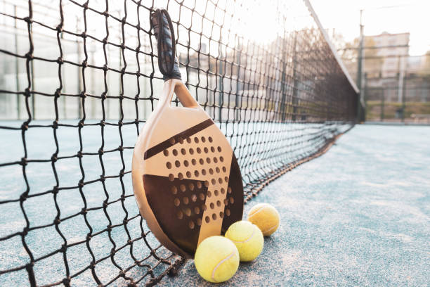 una raqueta y 3 pelotas de pádel junto a la red de la cancha. - tennis in a row team ball fotografías e imágenes de stock