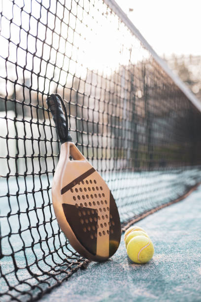 una raqueta y una pelota de pádel junto a la red de la pista. - tennis in a row team ball fotografías e imágenes de stock