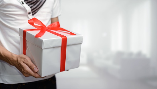 A selective focus shot of a man holding a present with a bow, in a white room, the concept of giving gifts for New Year, birthdays,and other occasions