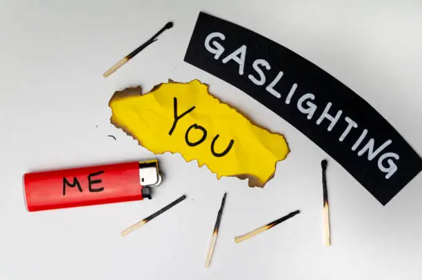 Word Gaslighting, on a black surface, next to a lighter with the word Me, and burnt yellow card with the writing You. Psychological meaning.