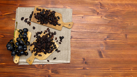 Black raisins with grapes on a wooden background, healthy snack, dietary product. Flat lay. Copy space