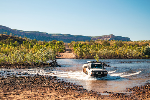 A 4x4 with a trailer crossing a wide river in The Kimberley in Western Australia during an off-road expedition.