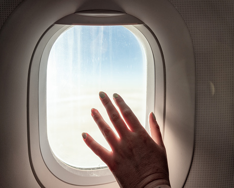A woman's hand on the window during an airplane journey, flying high above the clouds.