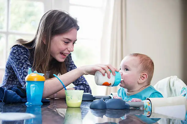 Photo of Girl feeding baby brother at table