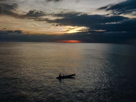 Thai Fisherman in typical small thai fishing longtail boat fishing during sunset in the Andaman Sea close to Khao Lac under moody dusk skyscape. Drone Point of View. Dramatic moody sunset over the Andaman Sea. Khao Lak, Andaman Sea, Phuket, Thailand, Southeast Asia.