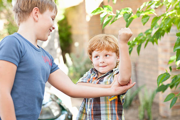 boy feeling brothers biceps outdoors - flexing muscles child little boys bicep foto e immagini stock