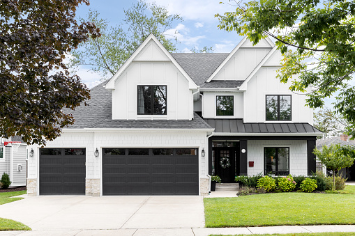 Oak Park, IL, USA - September 22, 2021: A luxury, white modern farmhouse with black framed windows, garage doors, and covered porch.
