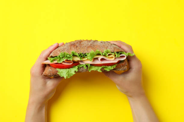 istock Female hands hold ciabatta sandwich on yellow background 1450654905